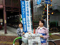 王子駅南口、雨の中、駅頭報告山崎たい子区議（右）